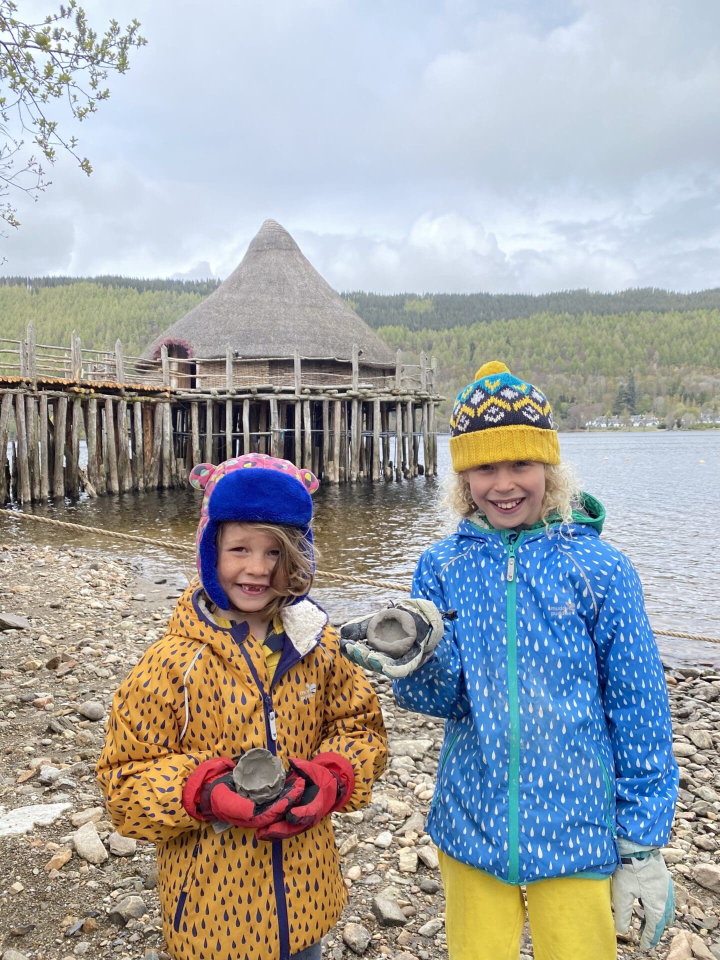 children holding clay bowls outside the Scottish crannog centre with blue and yellow jackets and hats on